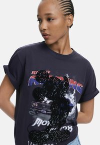 Schwarzes Baumwoll-T-Shirt mit umgeschlagenen Ärmeln, das ein Pailletten-Mickey-Mouse-Design und einen mehrfarbigen "Road Racing"-Grafikdruck zeigt.