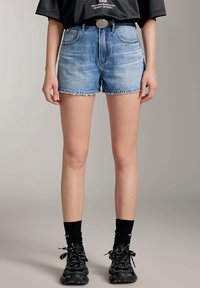 Ljusblå denimshorts med fransad nederkant, som har frontfickor och hög midja, kombinerat med svarta träningssneakers och strumpor.