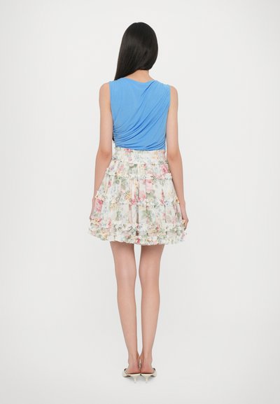 Blue sleeveless top with draped design paired with a floral print, ruffled mini skirt in light colors. Short, layered hemline, paired with heels.