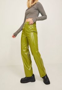 Zielone, błyszczące spodnie z sztucznej skóry o prostym kroju, w połączeniu z szarym crop topem z długim rękawem i masywnymi czarnymi platformami.
