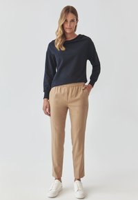 Marineblauwe lange mouw top gecombineerd met lichtbruine taps toelopende broek en witte sneakers. De stof lijkt zacht; de broek heeft een elastische tailleband.
