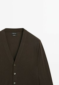 Brun cardigan med V-ringning, långa ärmar och fem silverknappar. Tillverkad av ett mjukt, texturerat tyg, lämplig för layering.