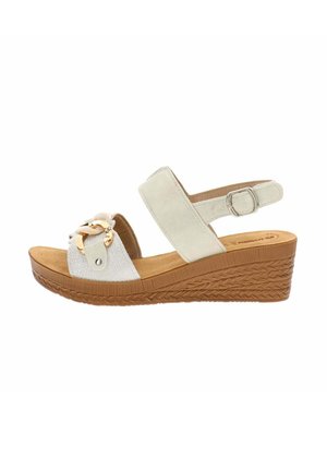 Sandale compensée beige avec boucle à la bride de cheville, bride avant décorée d’un détail chaîne dorée, et semelle marron texturée.