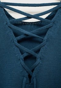 Mörk teal stickad topp med ett korsade spetsdetalj vid halsringningen, med en slät textur och en V-formad skärning.