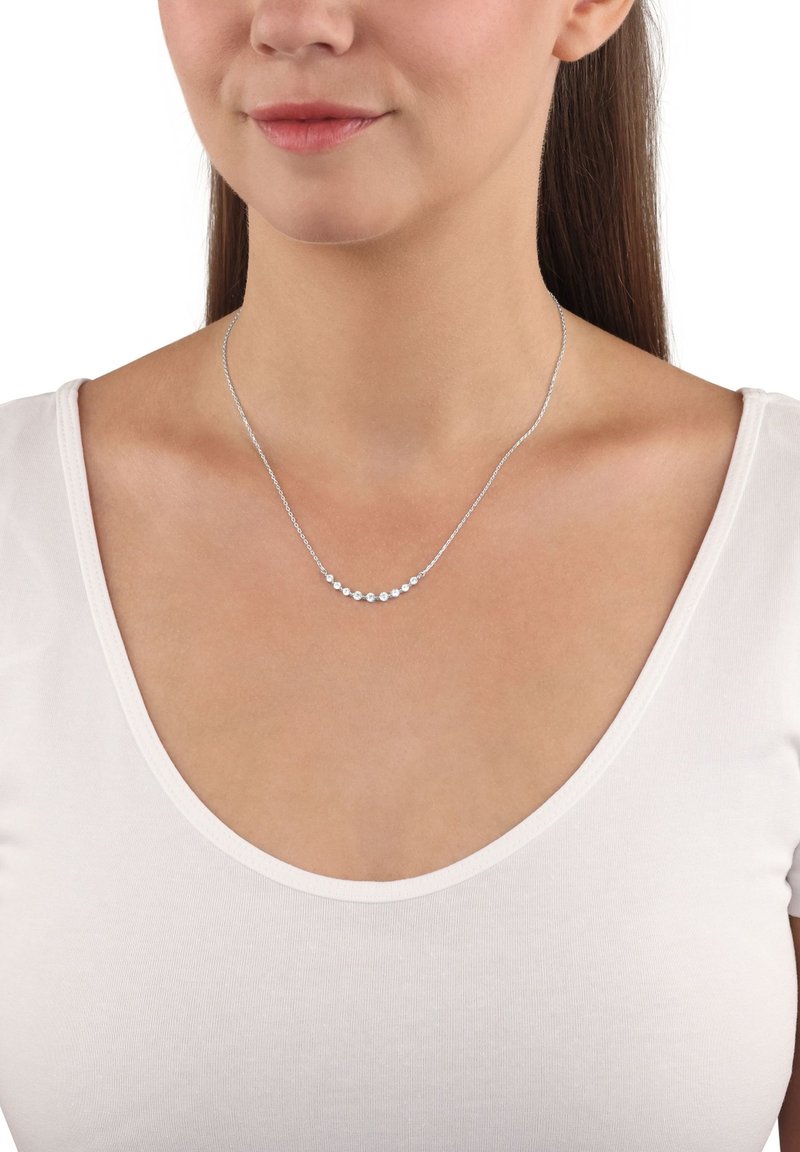 Collana in argento con cinque piccole pietre tonde, disposte in una leggera curva, su una maglietta bianca.