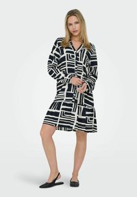 Sukienka koszulowa w granatowo-kremowym kolorze, z geometrycznymi wzorami, długimi rękawami, warstwowym dołem i luźnym krojem.