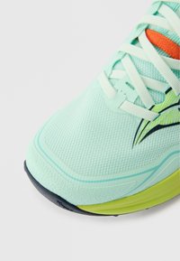 Ανοιχτό μπλε παπούτσι για τρέξιμο με άνω μέρος από διχτυωτό ύφασμα, υφή σε χρώμα μέντας, επίπεδα κορδόνια και μαύρη και λαχανί λαστιχένια σόλα.