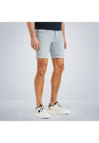 Helle blaue Denim-Shorts mit einer figurbetonten Passform, umgeschlagenen Säumen und einer glatten Textur. Kombiniert mit weißen Sneakers mit schwarzen Akzenten.