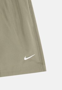 Nærbilde av olivengrønt stoff med sømmet kant og hvit Nike swoosh-logo nær kanten på en ensfarget bakgrunn.