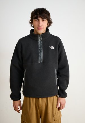 Sort fleece pullover med halvlukning, høj krave og hvidt logo på brystet. Har lynlåslommer i siden og tekstureret overflade.