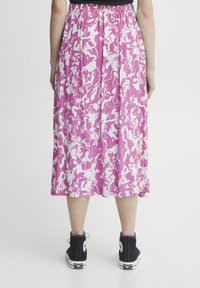 Falda midi floral con un patrón abstracto en rosa y blanco, cintura elástica, tela fluida, combinada con zapatillas altas negras.