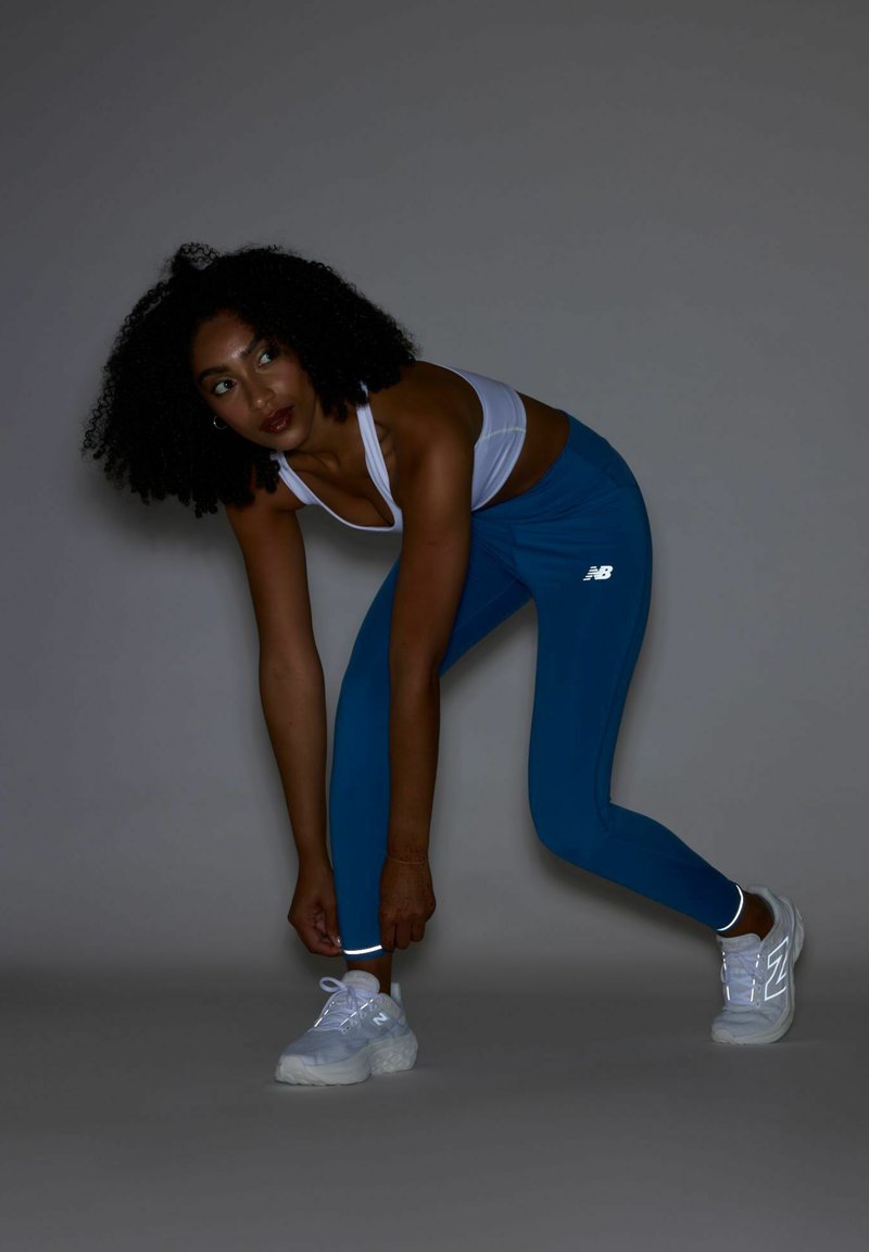 Leggings de sport bleus avec des accents réfléchissants, associés à un soutien-gorge de sport blanc et des baskets blanches, présentant un tissu texturé.