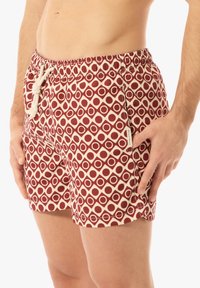 Červené a krémové plavky s elastickým pasem, přední kapsou a šňůrkou. Kulaté vzory vytvářejí geometrickou motiv. 