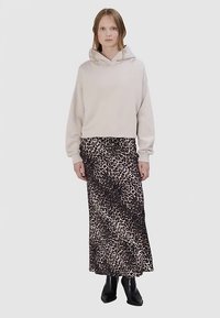 Lichtbeige cropped hoodie met een trekkoord, gecombineerd met een lange rok met luipaardprint. Model draagt zwarte enkellaarzen.
