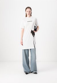 Balta per didelė marškinė su juodu tekstu ir juoda grafika, derinami su šviesiai mėlynomis plačiomis džinsomis ir juodais bateliais. Paprastas, kasdienis įvaizdis.