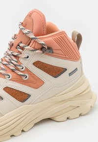 High-top sneaker featuring a peach upper with textured fabric panels, beige rubber sole, and contrasting laces in black and white patterns.