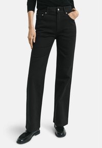 Jeans en denim noirs taille haute à jambe large, dotés de poches avant, de finitions en métal argenté et d'une texture lisse.