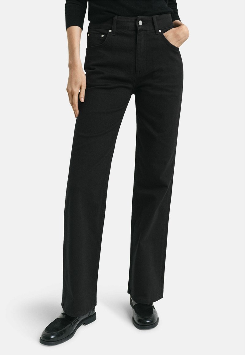 Jeans en denim noirs taille haute à jambe large, dotés de poches avant, de finitions en métal argenté et d'une texture lisse.