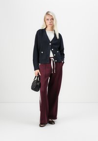 Navy knit cardigan with gold button accents and pockets, paired with burgundy wide-leg pants and leopard print flats. Black handbag included.