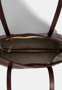 Braune Leder-Tote mit zwei Griffen, einem Reißverschluss-Innenfach und einer glatten Textur mit beigem Innenfutter. Innenansicht von oben.