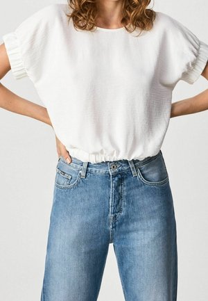 Weißes kurzärmeliges Oberteil mit gerafftem Saum, kombiniert mit hellblauen Denim-Jeans mit Vordertaschen und geradem Bein.