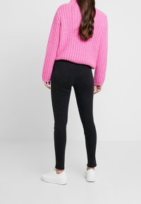 Jersey de punto rosa con cuello alto, combinado con jeans ajustados negros y zapatillas blancas. Los jeans tienen bolsillos traseros y un diseño ceñido.