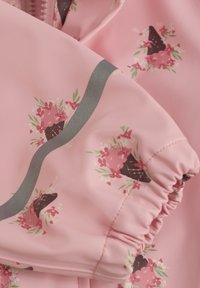 Rosa vandtæt stof med blomster-isvaffelmønster med grønne accenter. Inkluderer elastiske manchetter og en sølvkantdetalje.
