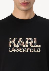 Juodas marškinėliai su tekstu "KARL LAGERFELD" daugiaspalviame argyle rašte, sudarytame iš kreminės, rudos ir juodos spalvos rombų, su apvalia iškirpte.