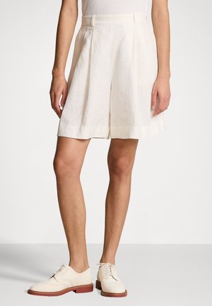 Shorts en lin blancs avec des plis, longueur mi-cuisse, et une ceinture. Associés à des chaussures oxford blanches et un haut ajusté texturé.