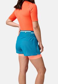 Tenue sportive comprenant un haut orange à manches courtes et un short bleu avec une doublure intérieure, mettant en avant un tissu respirant et des couleurs contrastantes.