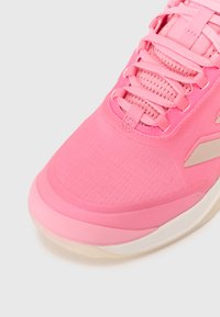 Athletic shoe with a predominantly pink fabric upper, featuring a smooth texture, intricate lacing system, and a contrasting white soles.