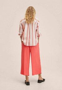 Gestreepte oversized blouse in lichtroze en wit, gecombineerd met brede koraalkleurige broeken, met een losse pasvorm en zachte stof. Zwarte sandalen met blokhak.
