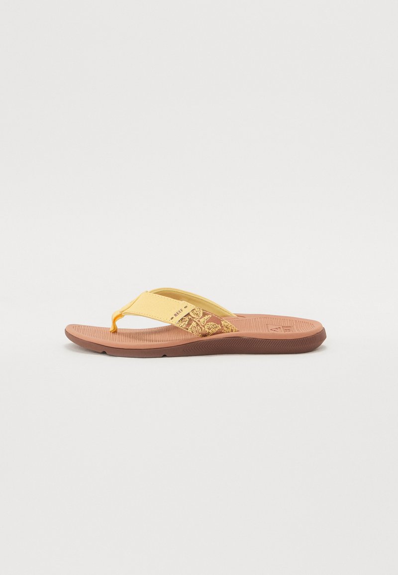 Sandale flip-flop galbene cu un model floral decorativ pe curea, talpă moale texturată și talpă din cauciuc maro. Post de deget ajustabil.