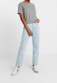 Grå t-shirt med kort ärm som matchas med ljusblå högmidjade raka jeans. Bärs med vita sneakers med svarta detaljer.