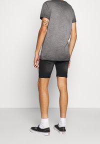 T-shirt gris, à manches courtes, dos légèrement allongé ; associé à un short en denim noir, des chaussettes blanches mi-mollet et des baskets noires.