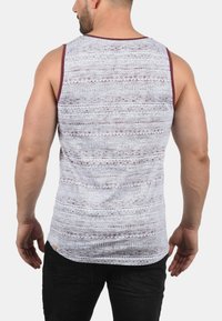 Hvit tanktopp med maroon aksenter, med et teksturert mønster av linjer og former. Glatt stoff, ermeløs design, normal passform.