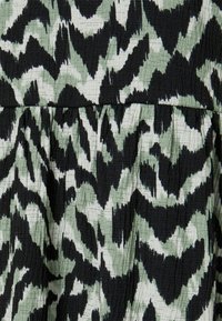 Strukturiertes Gewebe mit einem abstrakten Muster in Schwarz und Minzgrün mit wellenförmigen Linien. Das Material wirkt zerknittert und geschichtet.