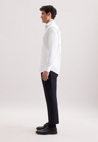 Camicia bianca a maniche lunghe con righe verticali, abbinata a pantaloni scuri e scarpe nere. Tessuto morbido, design elegante e silhouette aderente.