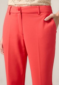 Koraalkleurige broek met een gladde textuur, voorzien van een enkele knoopsluiting, zijzakken en scherpe plooien voor een op maat gemaakte uitstraling.