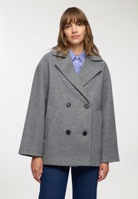 Szary wełniany płaszcz w stylu mieszanym z podwójnym zapięciem, szerokimi klapami, dwiema przednimi kieszeniami i czarnymi guzikami. W zestawie z niebieską koszulą w paski.