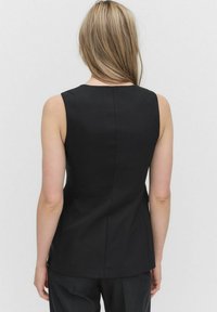 Svart ärmlös topp med en figurnära design, fållsömmar och mjuk textur, sedd bakifrån.