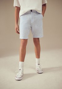 Modre in bele kratke hlače z gumbno zapirajo, stranskimi žepi, kombinirane z belimi nogavicami in klasičnimi belimi športnimi copati.