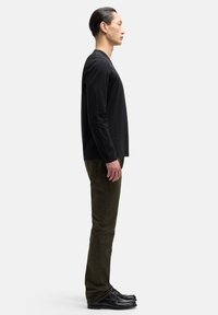 Czarna koszula z długim rękawem w połączeniu z oliwkowozielonymi spodniami i czarnymi butami. Strój cechuje się prostym, nowoczesnym designem i dopasowanym krojem.