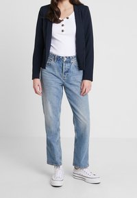 Námořnická blazer s puntíky přes bílý žebrovaný top s knoflíky, v kombinaci se světle modrými džíny rovného střihu a bílými teniskami.
