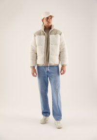 White, fluffy fleece jacket with beige accents, two front pockets, and a high collar. Paired with light blue jeans and cream sneakers.