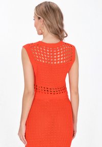 Abito a maglia di un vivace arancione con design senza maniche, motivo a fori aperti sul retro, texture a coste e silhouette aderente.