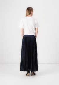 Mørkeblå plisseert maxi-skirt med elastisk midjebånd, kombinert med en ensfarget hvit t-skjorte og svarte høyhælte sko. Glatt tekstur og flytende design.