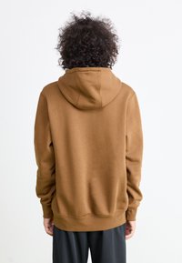 Brun hettegenser laget av mykt stoff, med snorhette, ribbestrikkede mansjetter og nederkant. Designet er enkelt uten synlige mønstre.