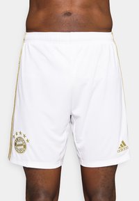 Vita atletiska shorts med guldaccenter, utrustade med FC Bayern München-logotypen och Adidas-märkning. Tillverkade av lätt och mjukt material.