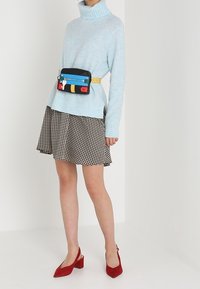 Ljusblå, randig polotröja i kombination med en svart- och vitrutig kjol. Accessoarer med en flerfärgad midjeväska och röda klackar.